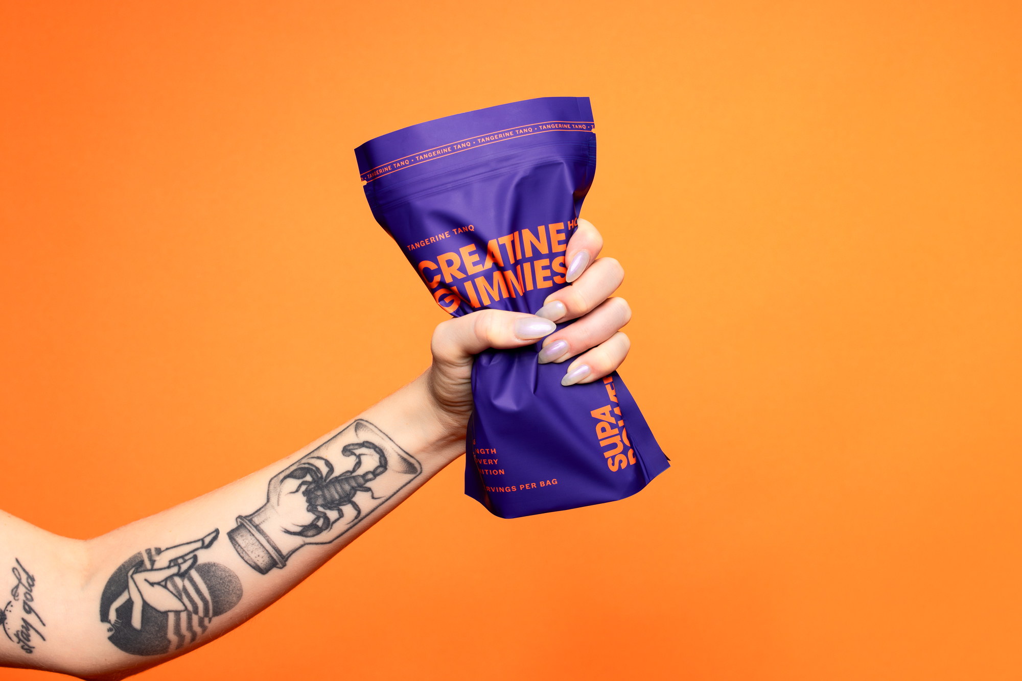 A tattooed arm gripping SUPA POWER tangerine creatine gummies